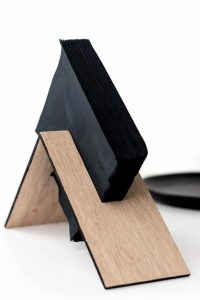 Geometric wooden napkin holder with black napkins on white background.